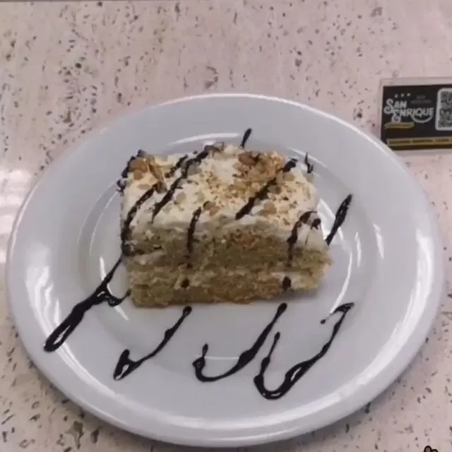 Porción de tarta con nata y nueces y chocolate por encima, en un plato blanco